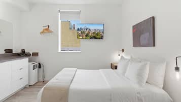A modern bedroom with a bed, a cityscape view, a white dresser, and a heater.