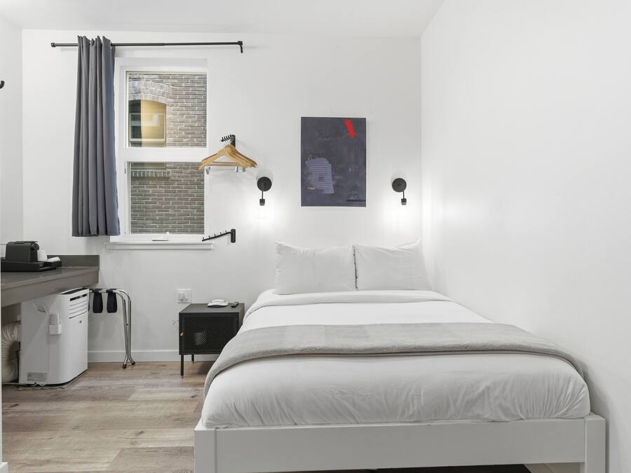 Quarto com cama, janela com cortina, luminária na parede, mesinha de cabeceira e aquecedor.