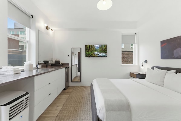 Une chambre d’hôtel moderne, équipée d’un lit, d’un bureau, d’un miroir, d’un tableau et offrant une vue sur l’extérieur.