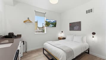 Un dormitorio moderno con cama, mesitas de noche, lámpara colgante, televisor montado en la pared y ventana con vistas.