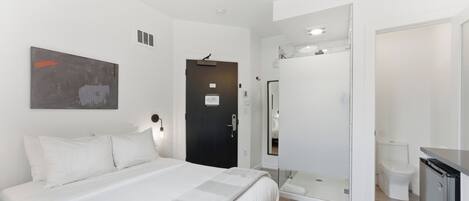 A modern hotel room with a bed, a shower, a toilet, and a small kitchenette.