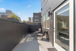 A modern balcony with seating, a glass door leading to a bedroom, and a cityscape view. - The Boylston Hotel Capitol Hill (Seattle)