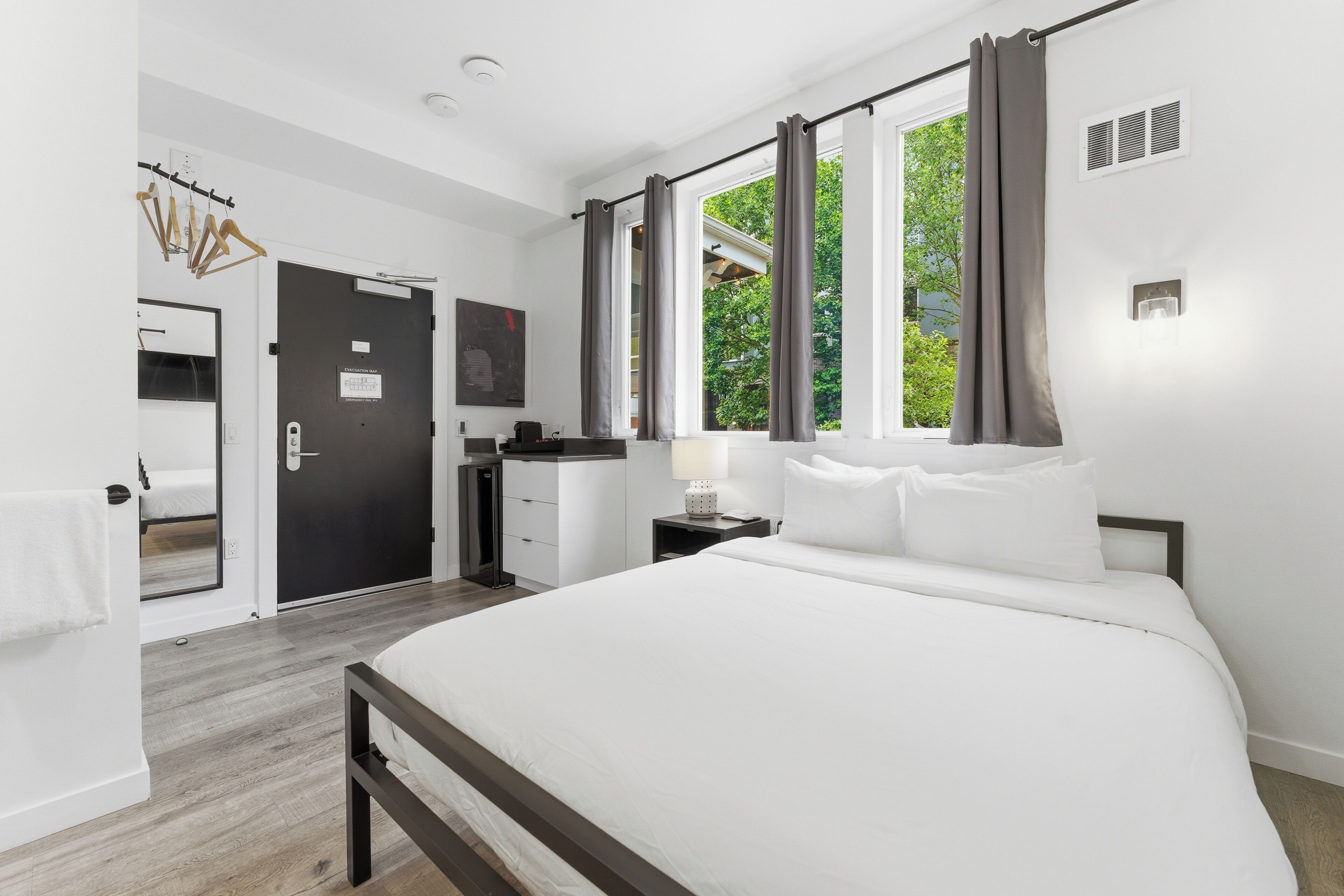 A bedroom with a bed, a dresser, a mirror, a door, and a window with curtains.