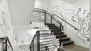 Un escalier avec des rampes noires et des marches en bois, agrémenté de décorations murales comprenant des notes de musique et des instruments.