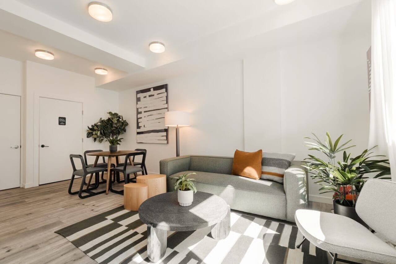Een moderne woonkamer met een grijze bank, een ronde salontafel, en een eethoek met een tafel en stoelen.