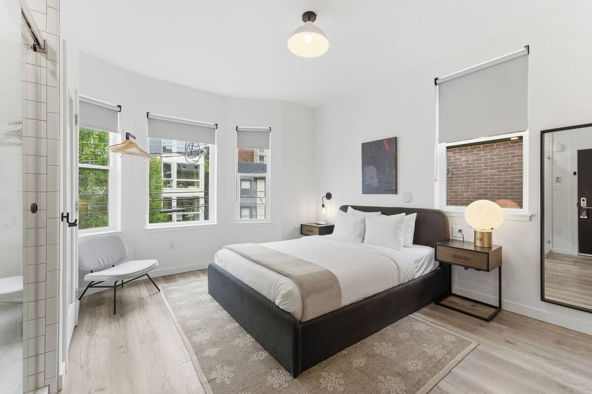 Une chambre à coucher avec un lit, des tables de chevet, une chaise, une fenêtre et un miroir.