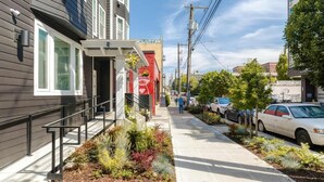 Un bâtiment moderne doté d’un auvent rouge et d’un petit espace jardin agrémenté de diverses plantes.