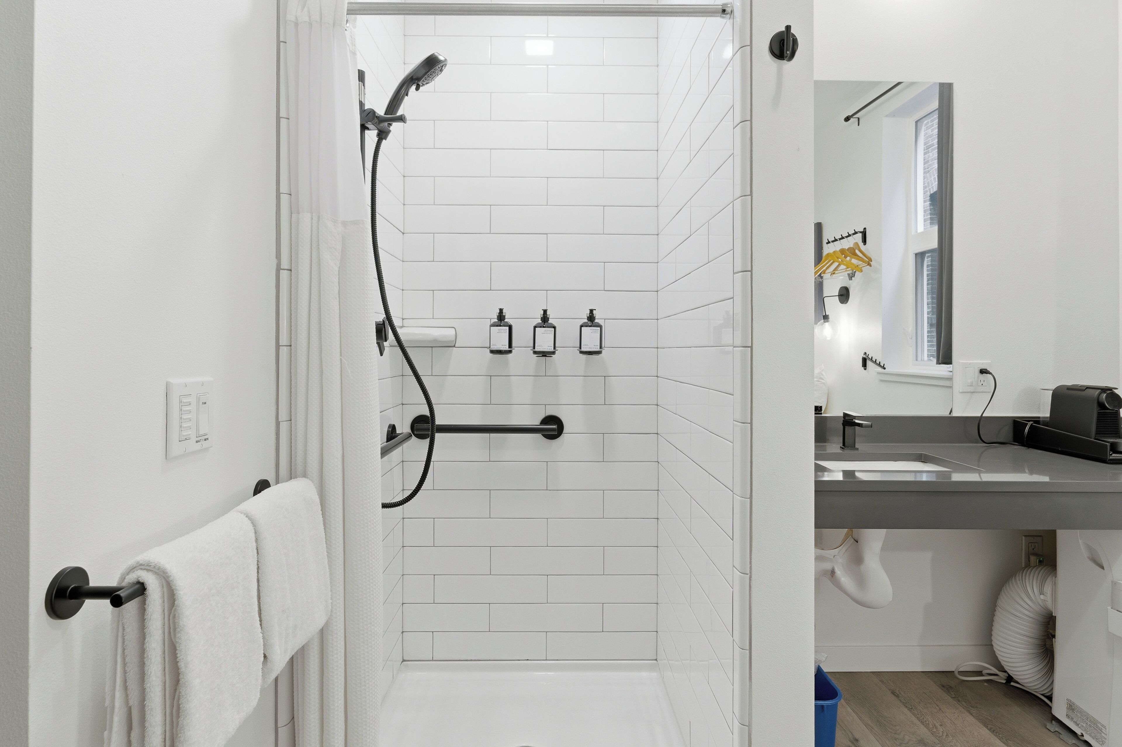 A modern bathroom with white tiles, a shower with a handheld showerhead, a towel rack, and a sink with a mirror.