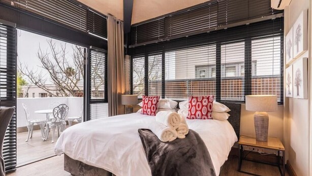 A hotel room with a large bed, a nightstand, a lamp, and a view of the outside. - Avemore Eikehof No 2 (Stellenbosch)