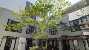 A modern building with a sign for 'Nails' on the right, a 'Rampper' sign on the left, and a courtyard with trees and benches. - Avemore Eikehof No 2 (Stellenbosch)