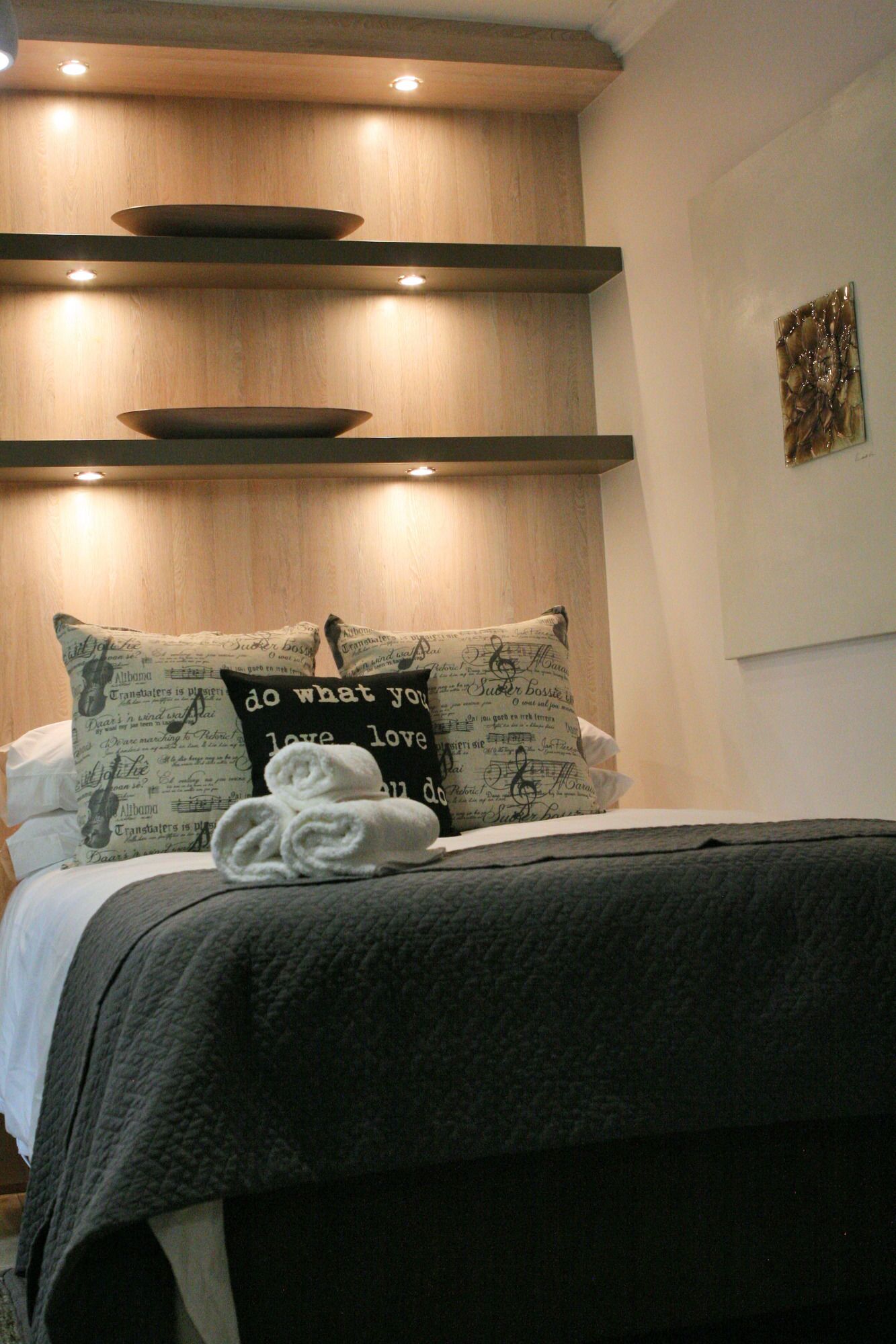 A neatly made bed with a dark gray comforter and pillows with musical notes and text.
