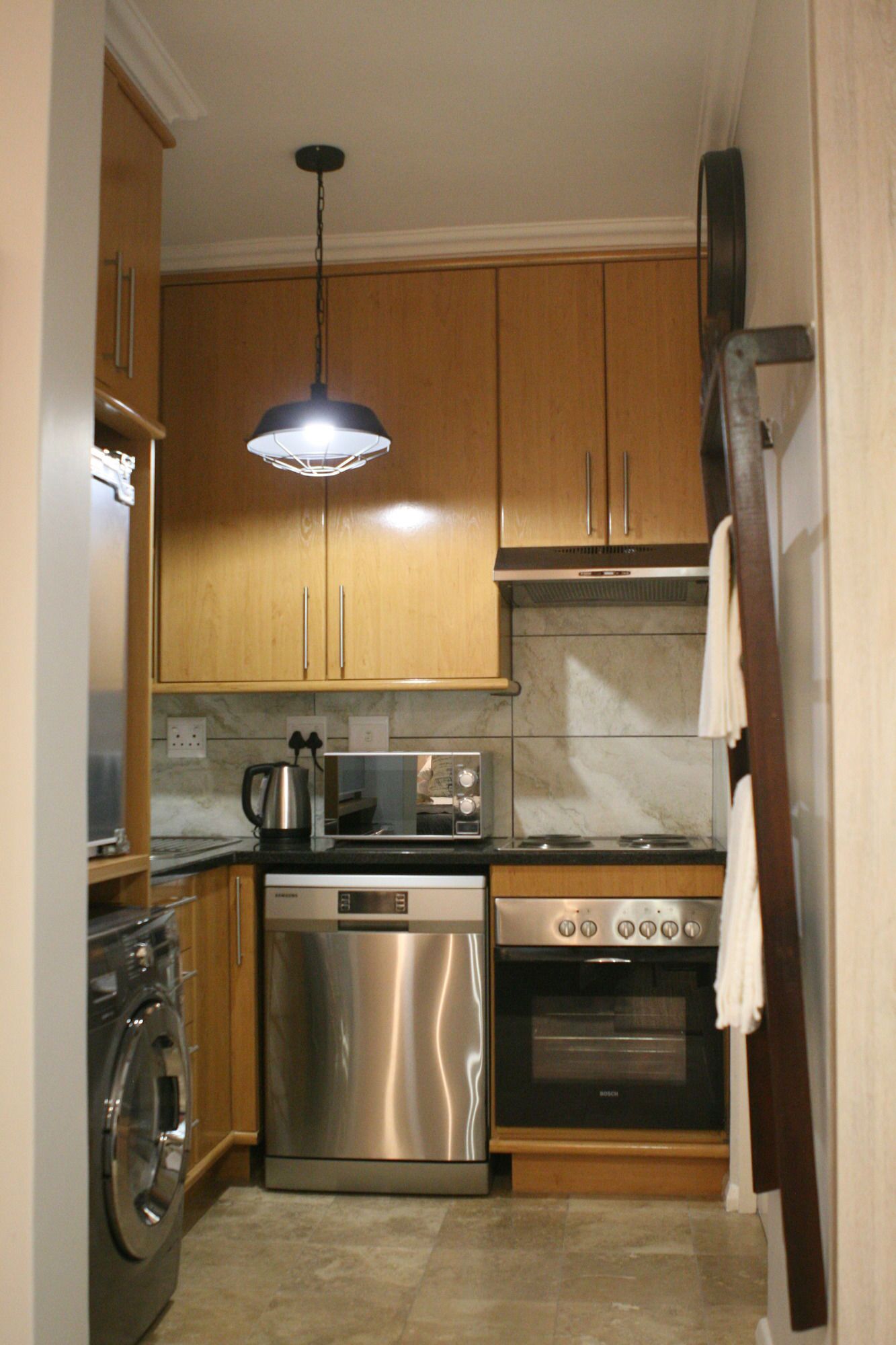 A compact kitchen with wooden cabinets, a stainless steel dishwasher, a microwave, a toaster, a stove, and a washing machine.