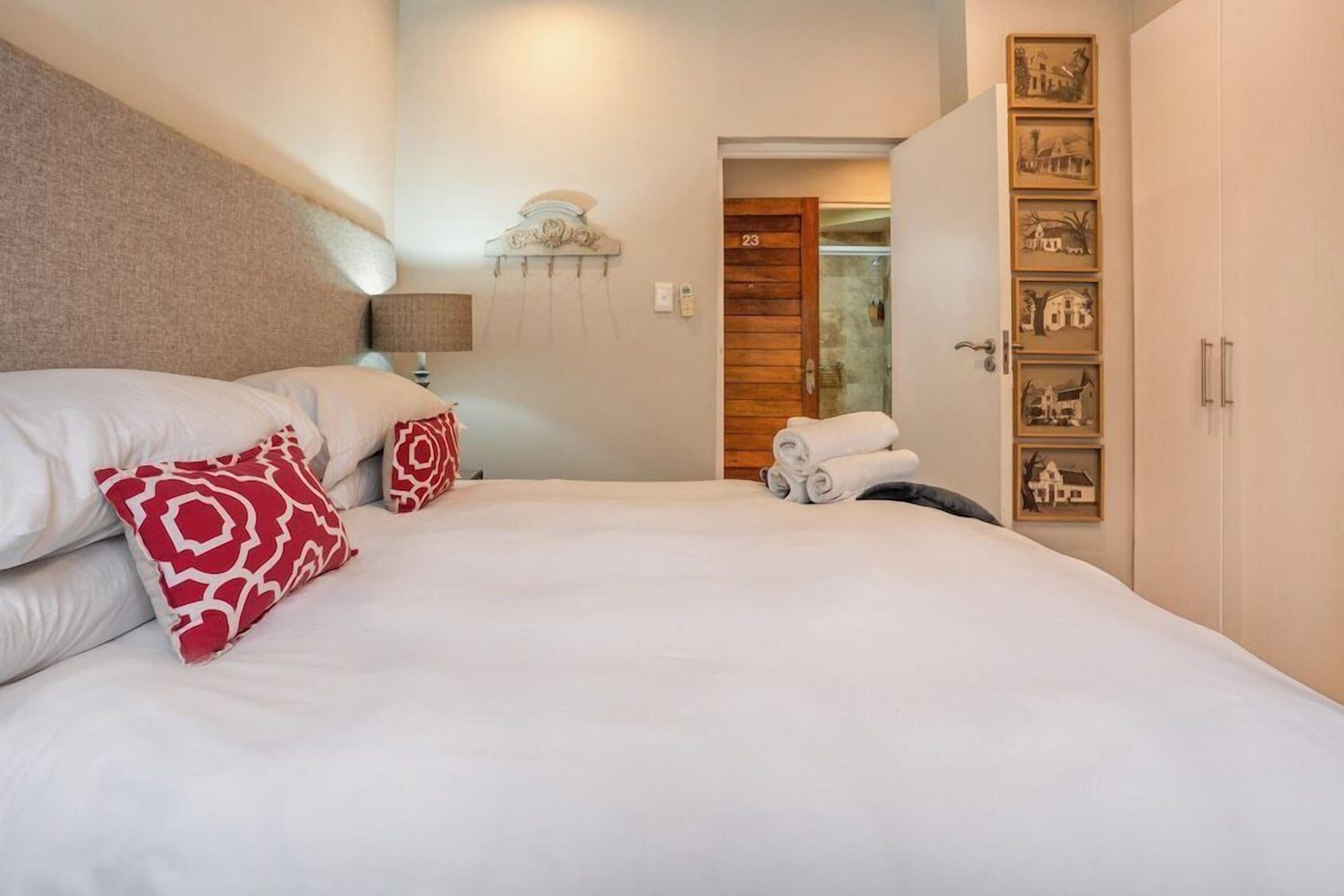 Habitación de hotel con una cama grande, una mesita de noche con lámpara, una puerta de madera y una pared con cuadros enmarcados.