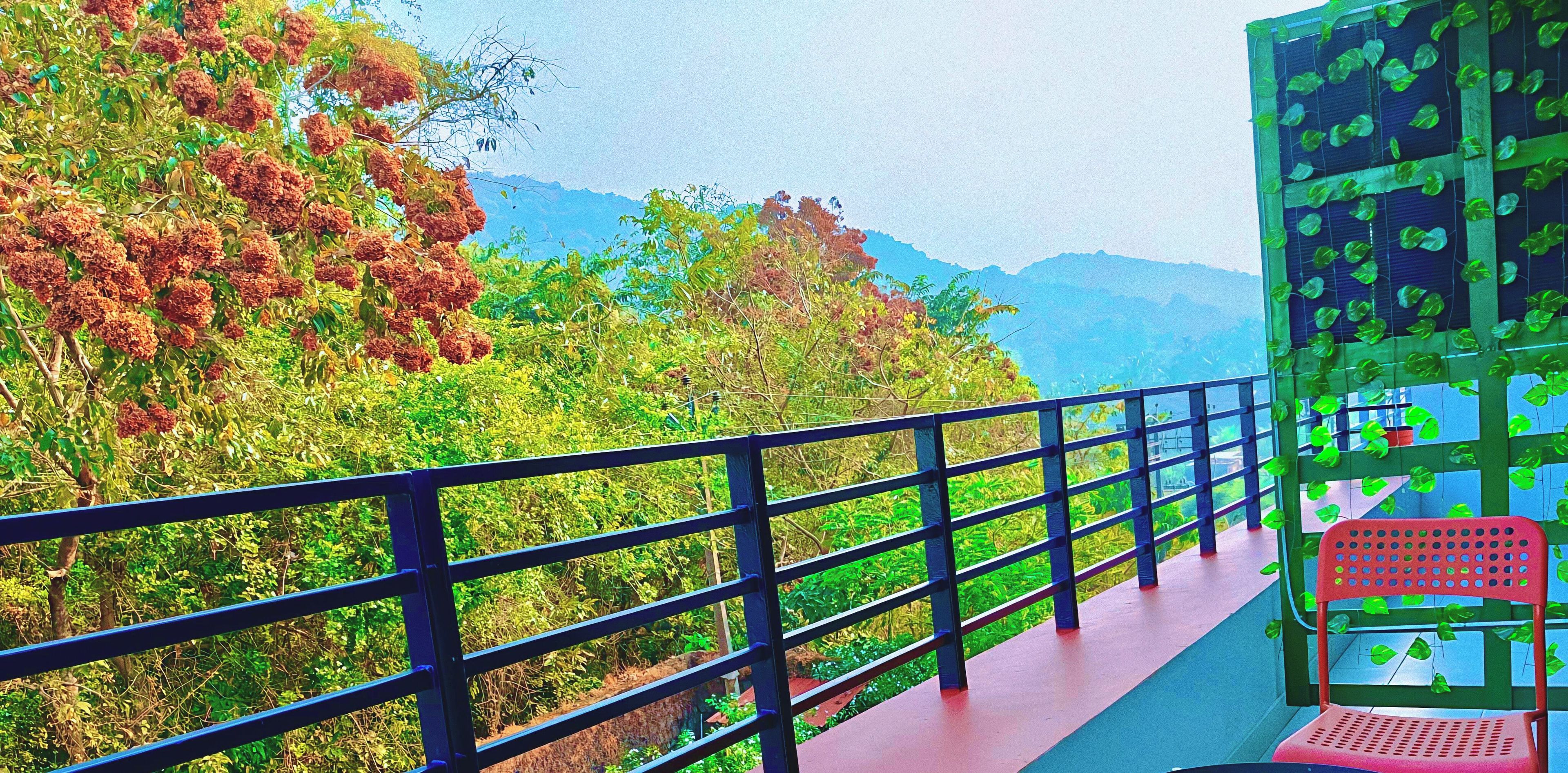 A balcony with a metal railing overlooking a lush landscape with trees and mountains.