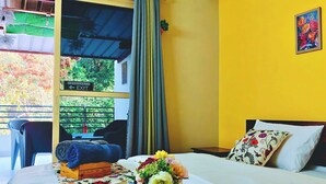 Habitación de hotel con cama, una pequeña mesa con sillas, ventana con señal de salida de emergencia y vista a zonas verdes.