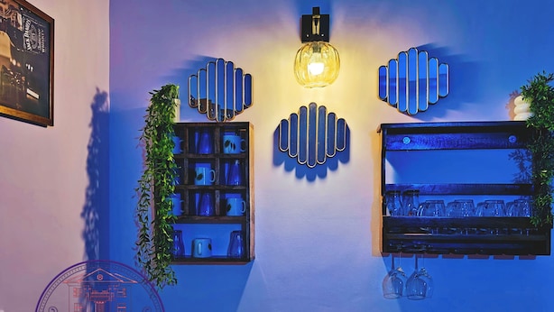 Una pared con decoración azul, un cuadro enmarcado, una estantería con tazas, una lámpara colgante y el logotipo de 'Retiro Urbano'.