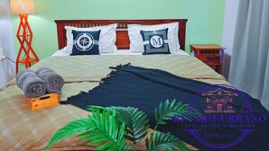 Un dormitorio con cama, almohadas, una mesita de noche, una lámpara y decoración en la pared.