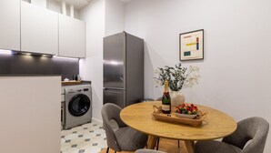 A compact kitchen with a washing machine, a refrigerator, and a dining area with a table set for two. - Bright 2-Bed Apartment in Las Letras, Madrid (Madrid)