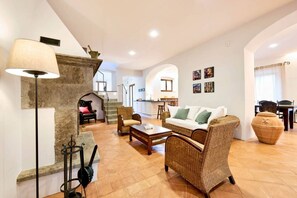 A spacious living area with a fireplace, wicker furniture, and a kitchen in the background. - Villa Beltramonto by MMega (Tuscany)