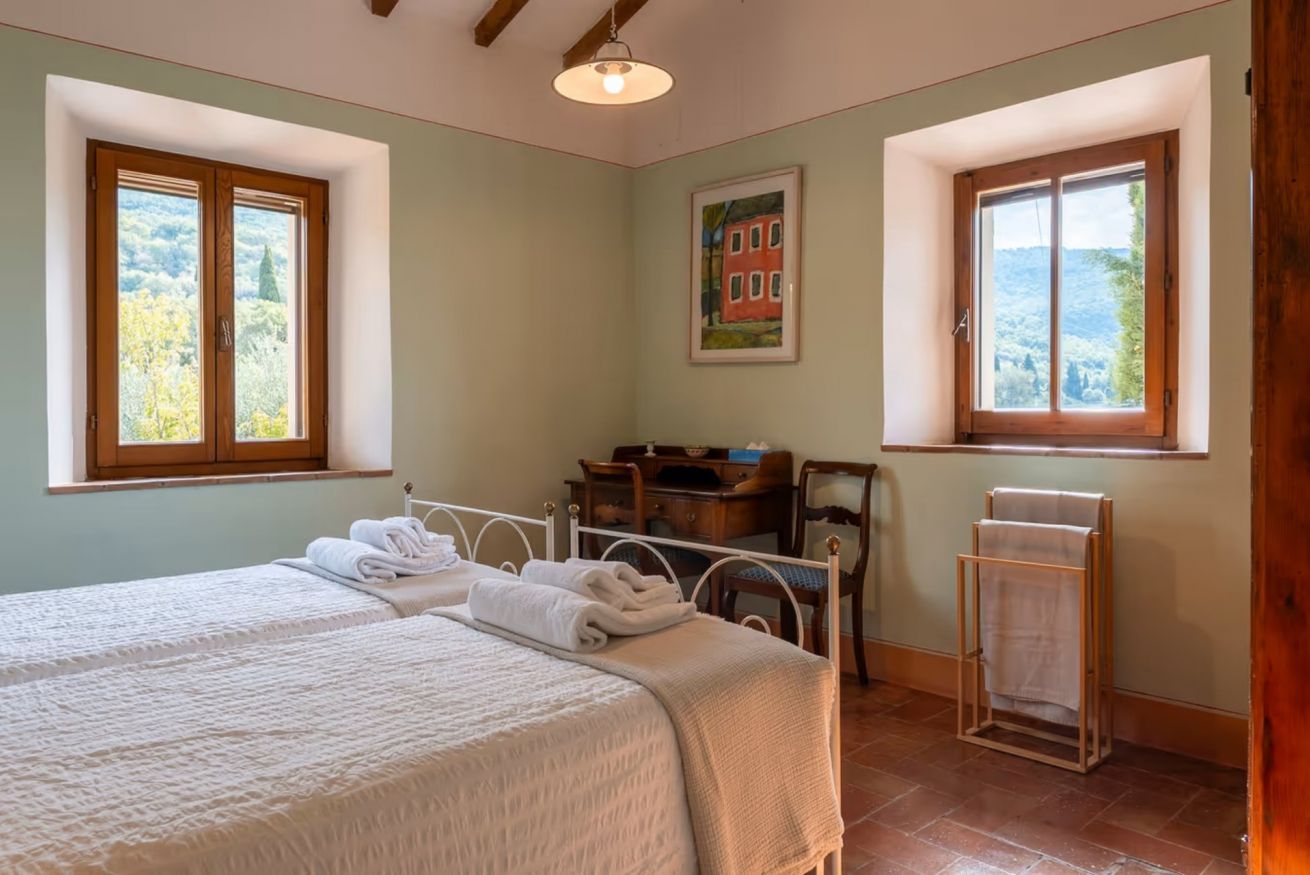 A bedroom with two beds, a desk, a chair, and a window with a view.