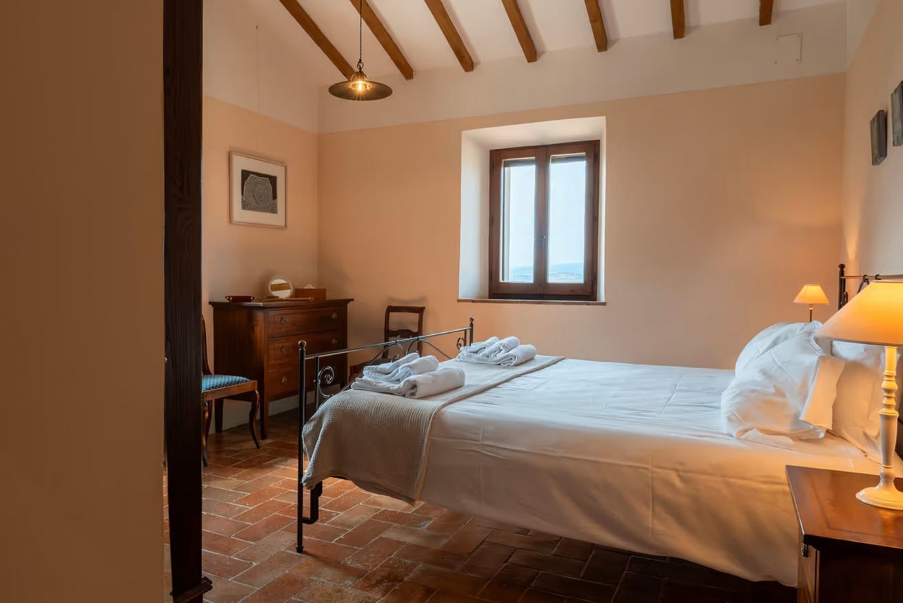 Een slaapkamer met een bed, een bureau, een stoel, een raam en een lamp.