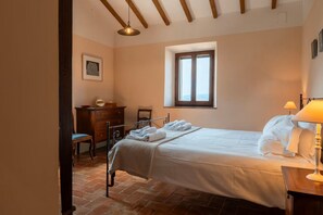 A bedroom with a bed, a desk, a chair, a window, and a lamp.
