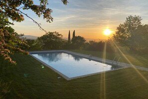 A rectangular swimming pool surrounded by grass, with a sunset in the background. - Villa Beltramonto by MMega (Tuscany)