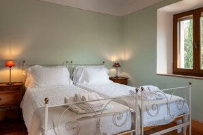 A double bed with white bedding, two bedside tables with lamps, a window with a view of trees, and a wooden floor. - Villa Beltramonto by MMega (Tuscany)