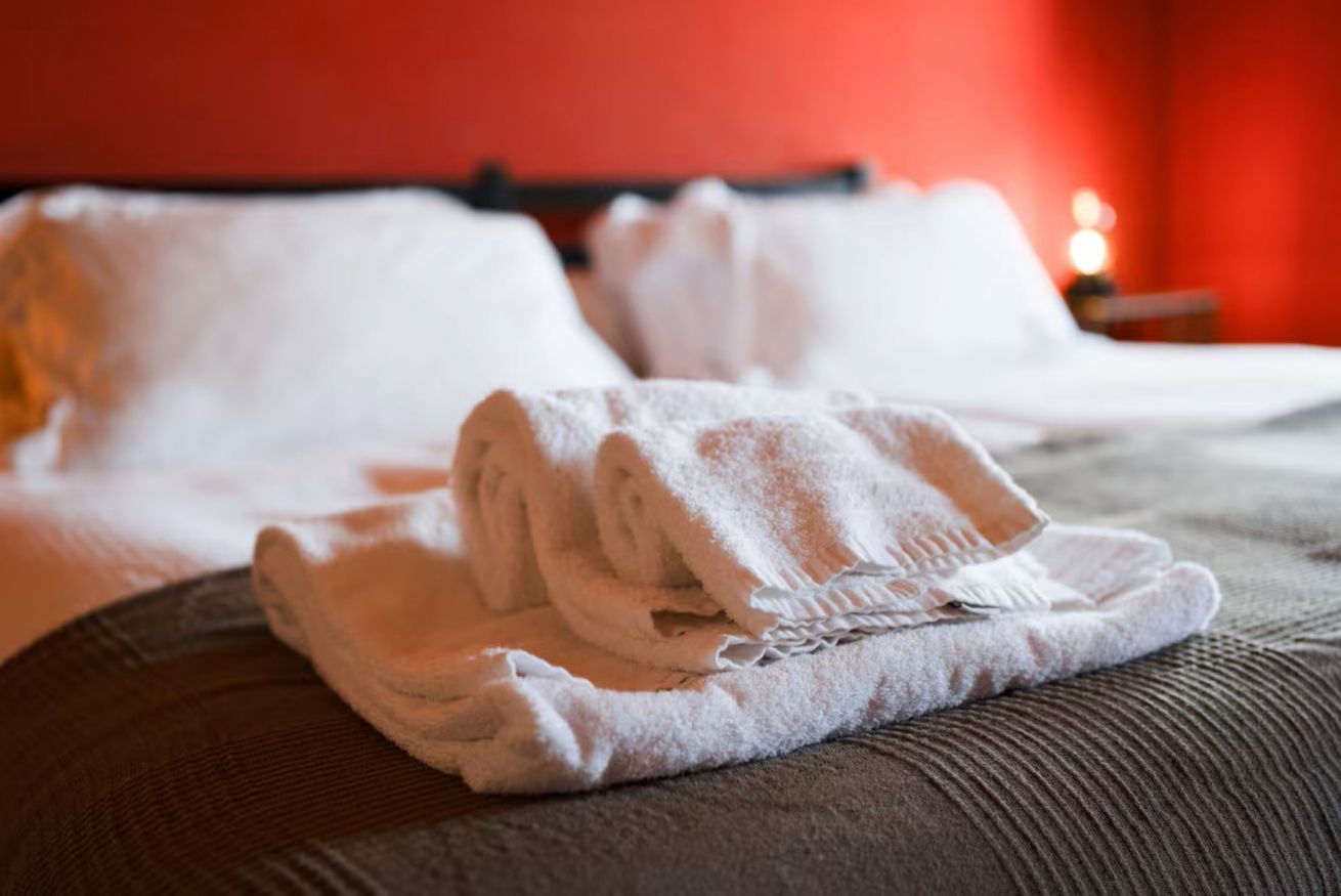 A neatly made bed with white linens and a folded towel on a brown pillow.