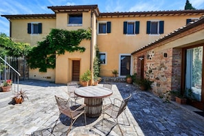 A courtyard with a wooden table and chairs, potted plants, and a building with a stone facade. - Villa Beltramonto by MMega (Tuscany)