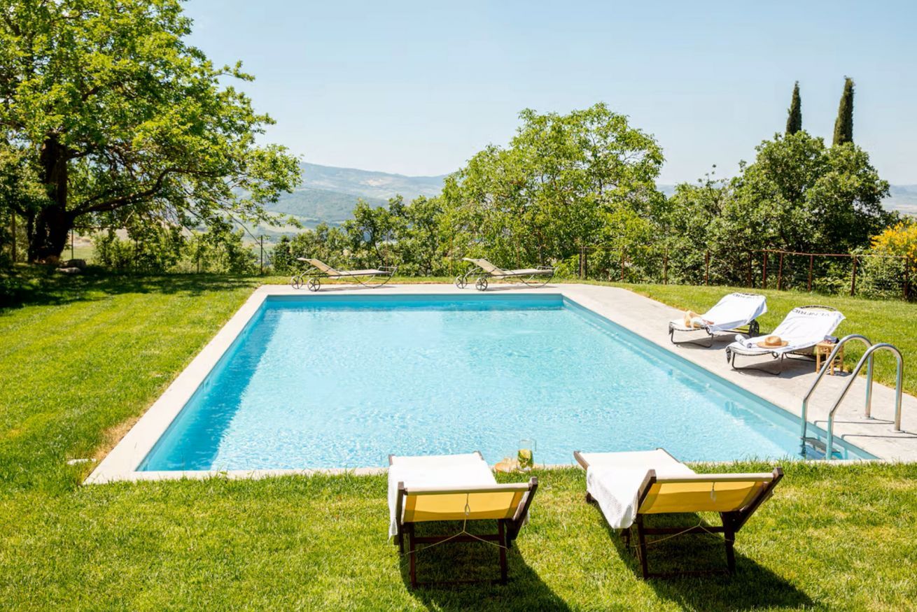 A rectangular swimming pool with a clear blue water surface, surrounded by a well-maintained lawn and trees.