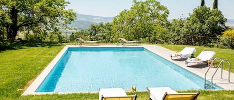 A rectangular swimming pool with a clear blue water surface, surrounded by a well-maintained lawn and trees.