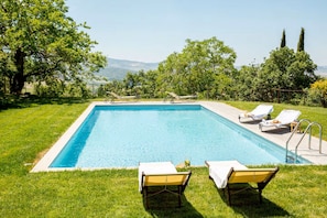 A rectangular swimming pool with a clear blue water surface, surrounded by a well-maintained lawn and trees.