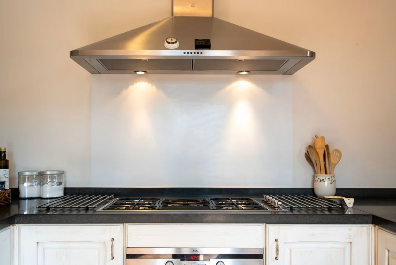 Une cuisine équipée d’une hotte en acier inoxydable, d’une cuisinière à gaz et de meubles blancs.