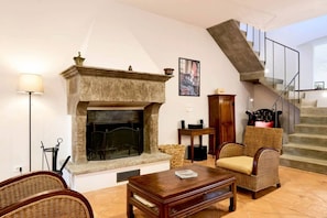 A living room with a fireplace, a staircase, wicker furniture, and a framed picture on the wall. - Villa Beltramonto by MMega (Tuscany)