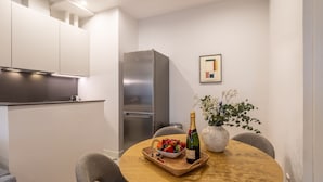 Una cocina moderna con refrigerador empotrado, una mesa de comedor con una cesta de frutas y una botella de champán, y una planta en maceta en la pared.