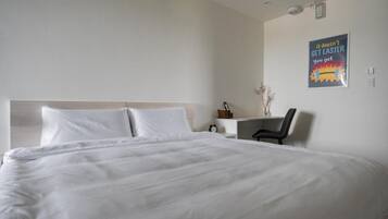 Habitación de hotel con una cama grande, un escritorio y una silla. Hay un cartel en la pared.