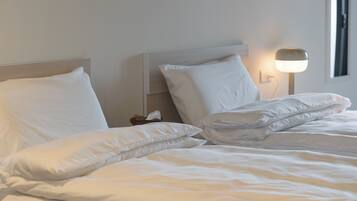A neatly made bed with white linens and pillows, a bedside table with a lamp, and a window with natural light.