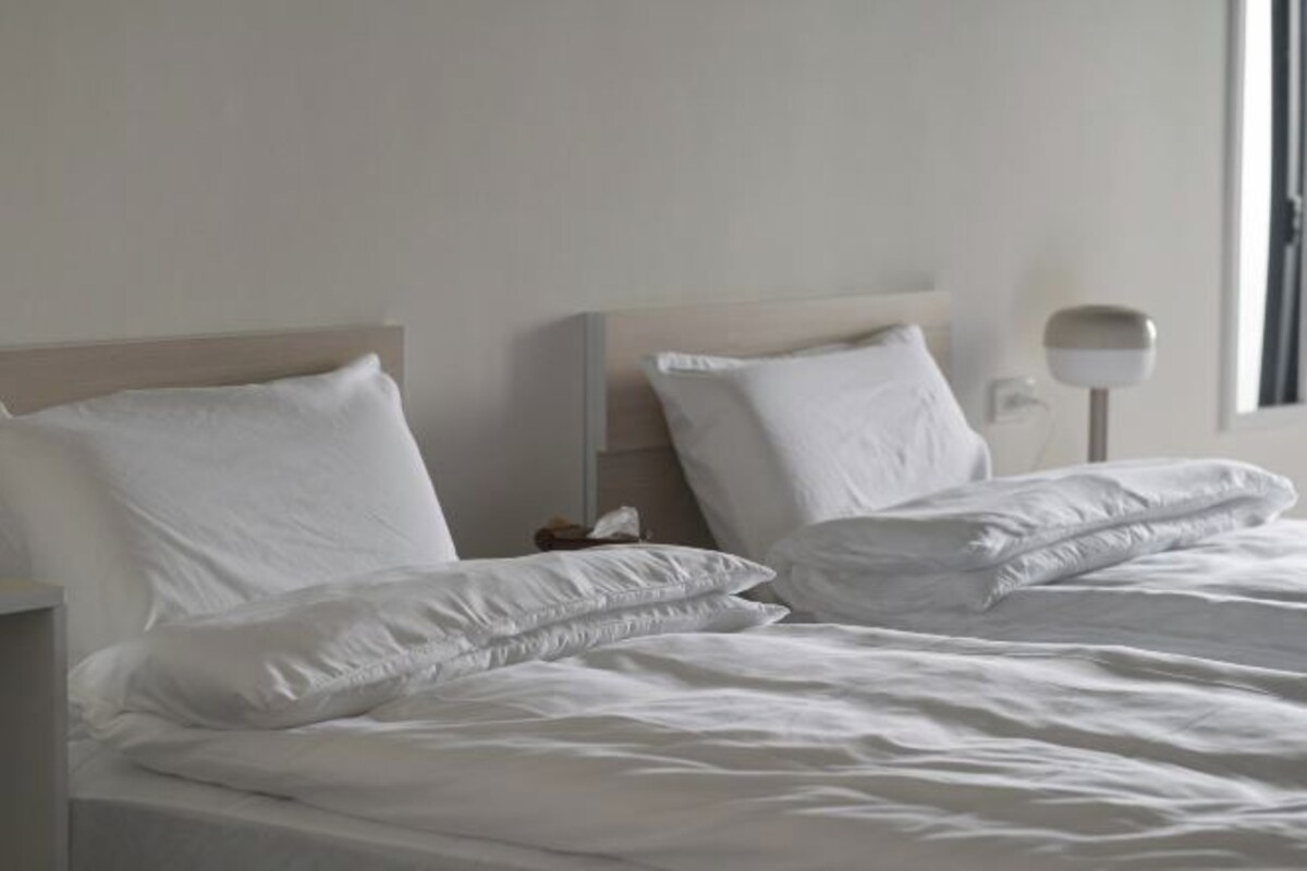 A hotel room with a bed, pillows, a nightstand, and a lamp.