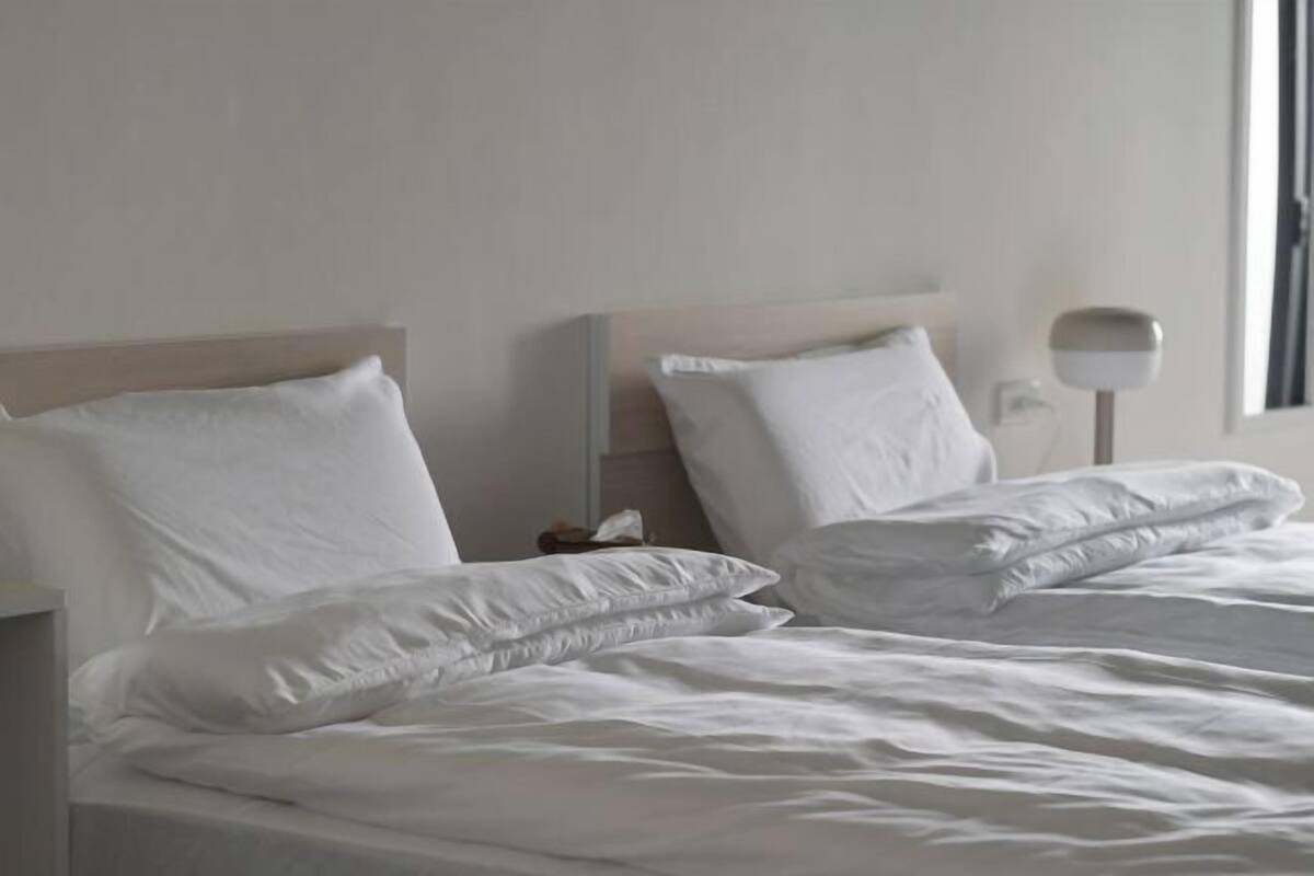 Una habitación de hotel con una cama, almohadas, una mesita de noche y una lámpara.