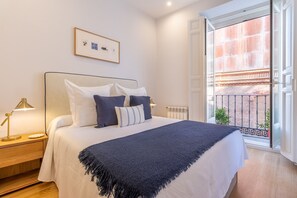 Une chambre à coucher avec un lit, des lampes de chevet, un tableau encadré au mur et une vue sur un balcon doté d’une balustrade.