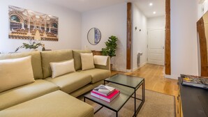 A living room with a beige sofa, a glass coffee table, and a bookshelf. - Elegant Apartment in Las Letras (Madrid)