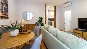 A modern living room with a round wooden dining table, a grey sofa, and a television on a stand. - Elegant Apartment in Las Letras (Madrid)