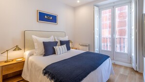 A bedroom with a bed, bedside lamp, and a window with a view of a brick wall. - Elegant Apartment in Las Letras (Madrid)