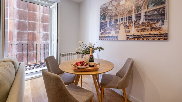 A dining area with a round table, two chairs, a vase with flowers, and a basket of fruit. - Elegant Apartment in Las Letras (Madrid)