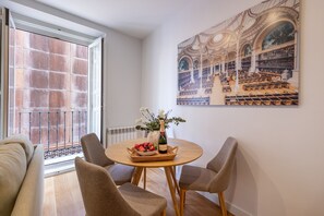 Een eetgedeelte met een ronde tafel, twee stoelen, een vaas met bloemen en een mand met fruit.