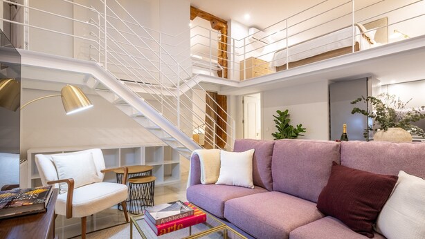 Een moderne woonkamer met een bank, stoelen, een salontafel en een trap.