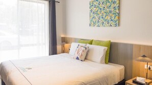 A hotel room with a large bed, a bedside table with a lamp, a small drawer, and a wall-mounted artwork. - Port Fairy Motor Inn (Port Fairy)