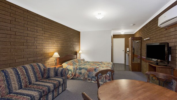 A hotel room with a brick wall, a bed with a colorful quilt, a sofa, a wooden table, and a television. - Port Fairy Motor Inn (Port Fairy)