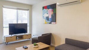 A modern living room with a flat-screen TV, a wooden coffee table, a grey sofa, and a colorful abstract painting on the wall. - Port Fairy Motor Inn (Port Fairy)